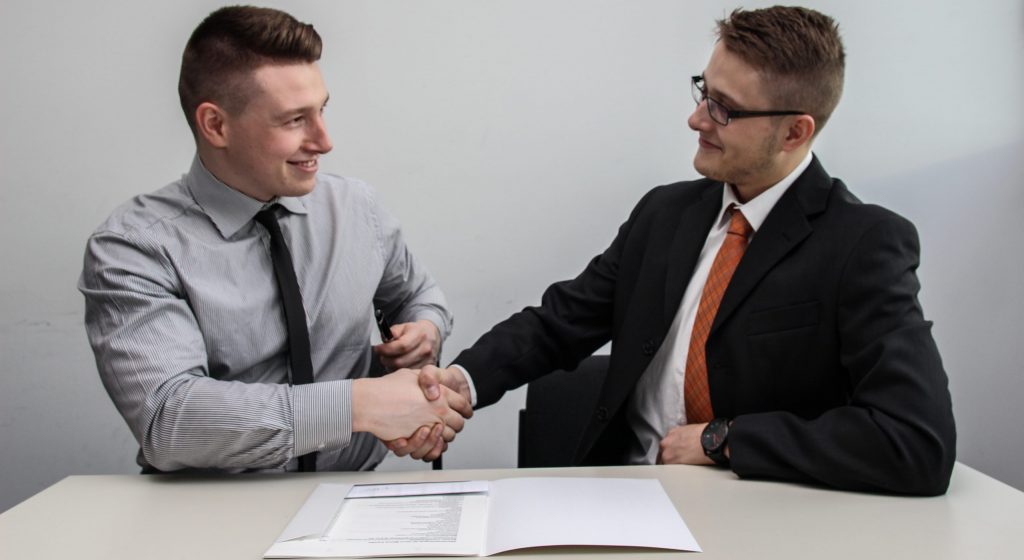 two men facing each other while shake hands and smiling