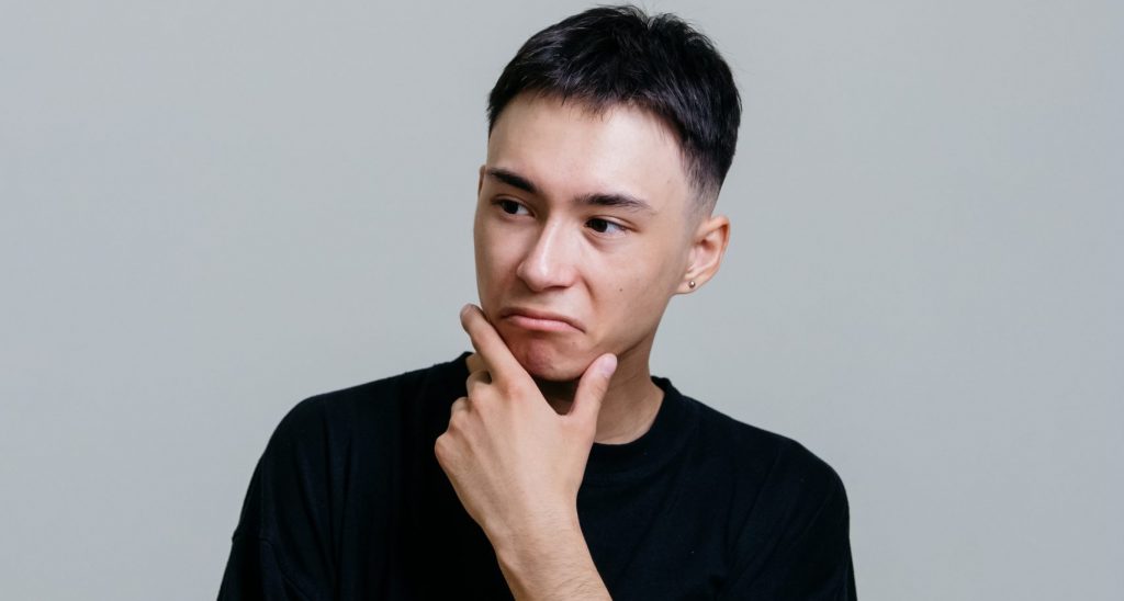 Man in black crew neck shirt thinking with his hand on his chin