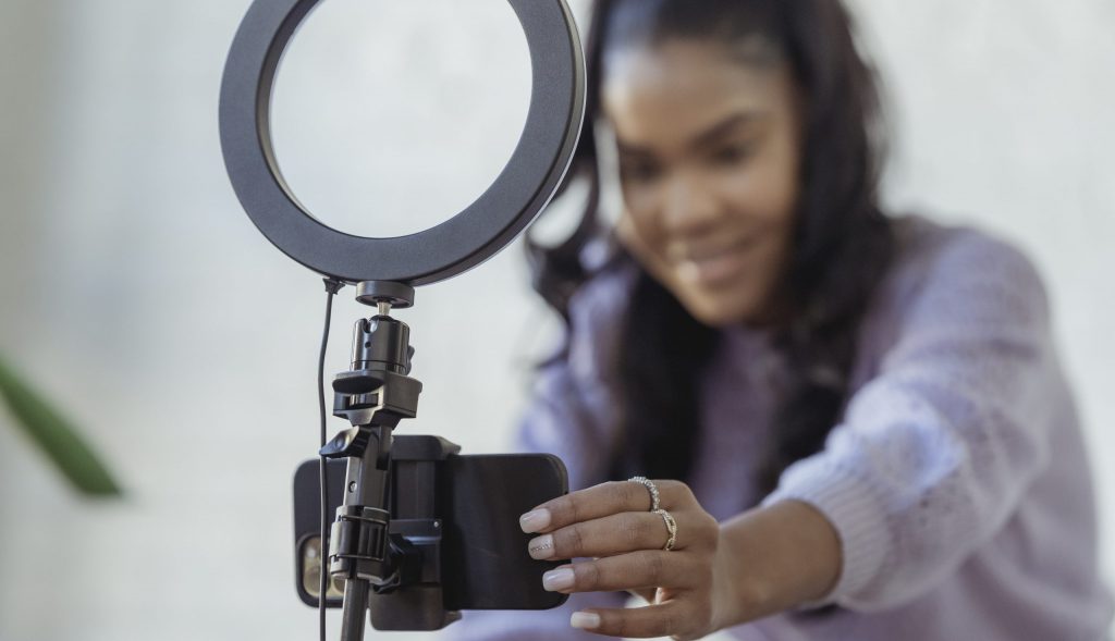 Happy young black woman setting up smartphone before shooting podcast