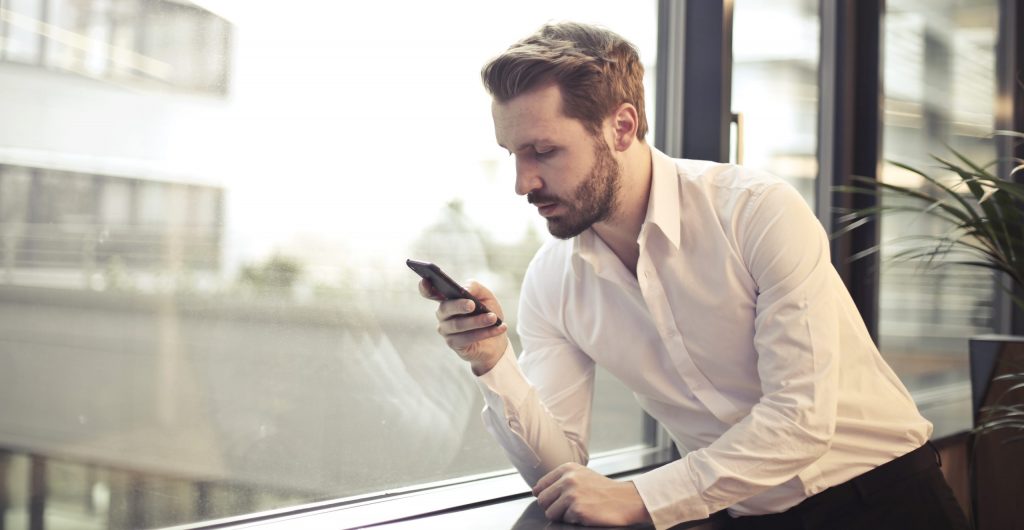 Photo of man in white dress shirt holding phone near window