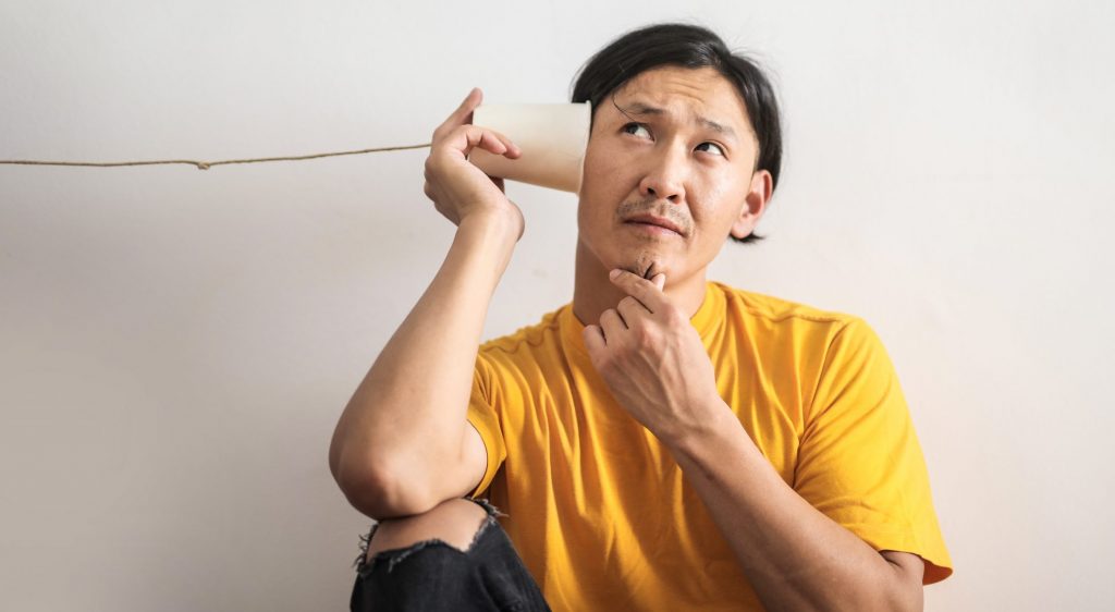 Pensive ethnic man listening to answer in paper cup phone