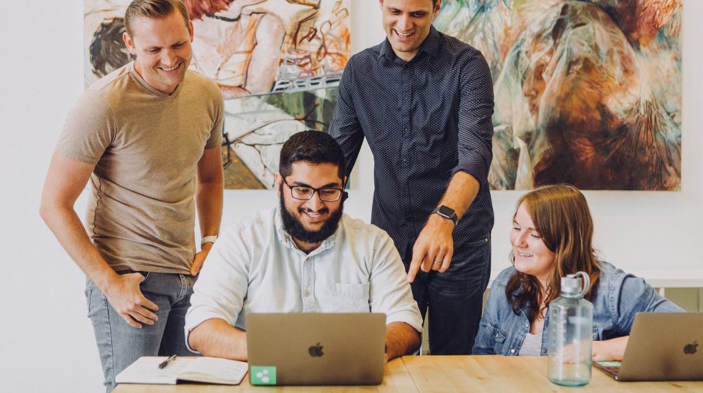 Design review in startup office with macbook and artwork. Man wearing Apple Watch. Joyful team working together and laughing.