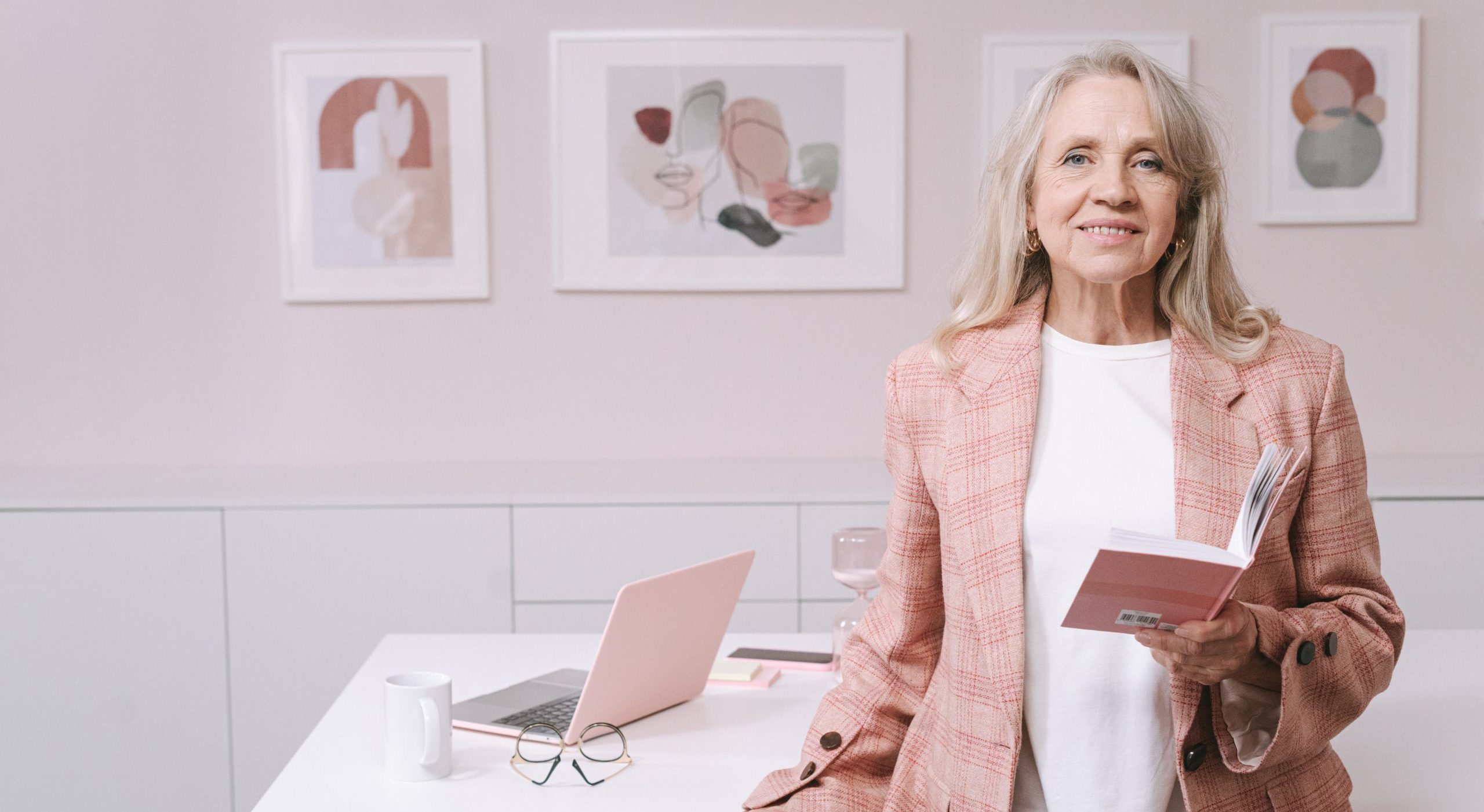 An elderly woman in pink blazer smiling while holding a book