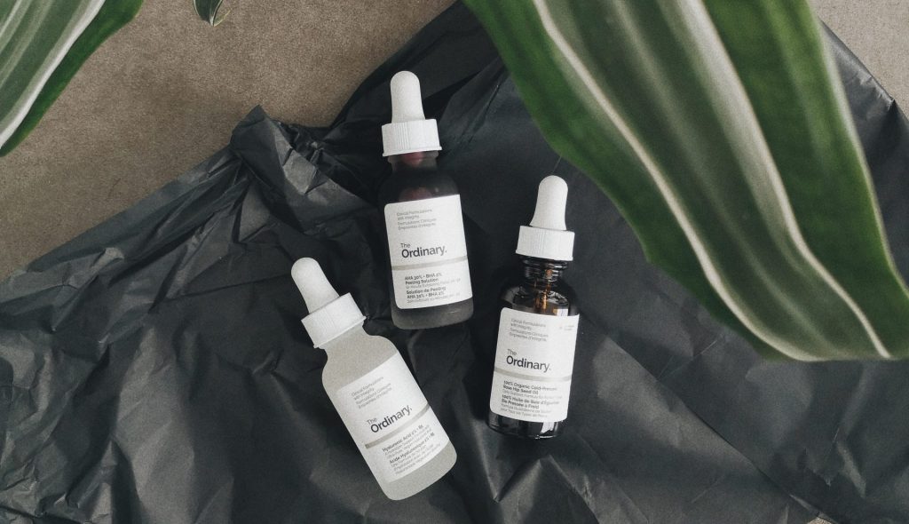 The Ordinary skincare product shot on a black background with a plant.