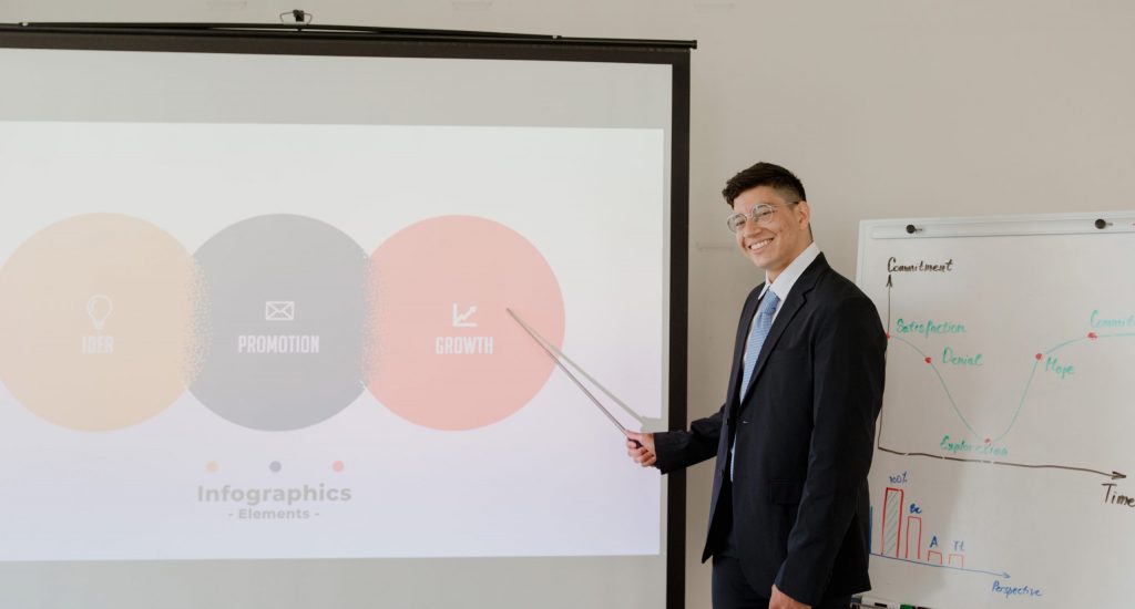 Man in black suit standing beside projector screen